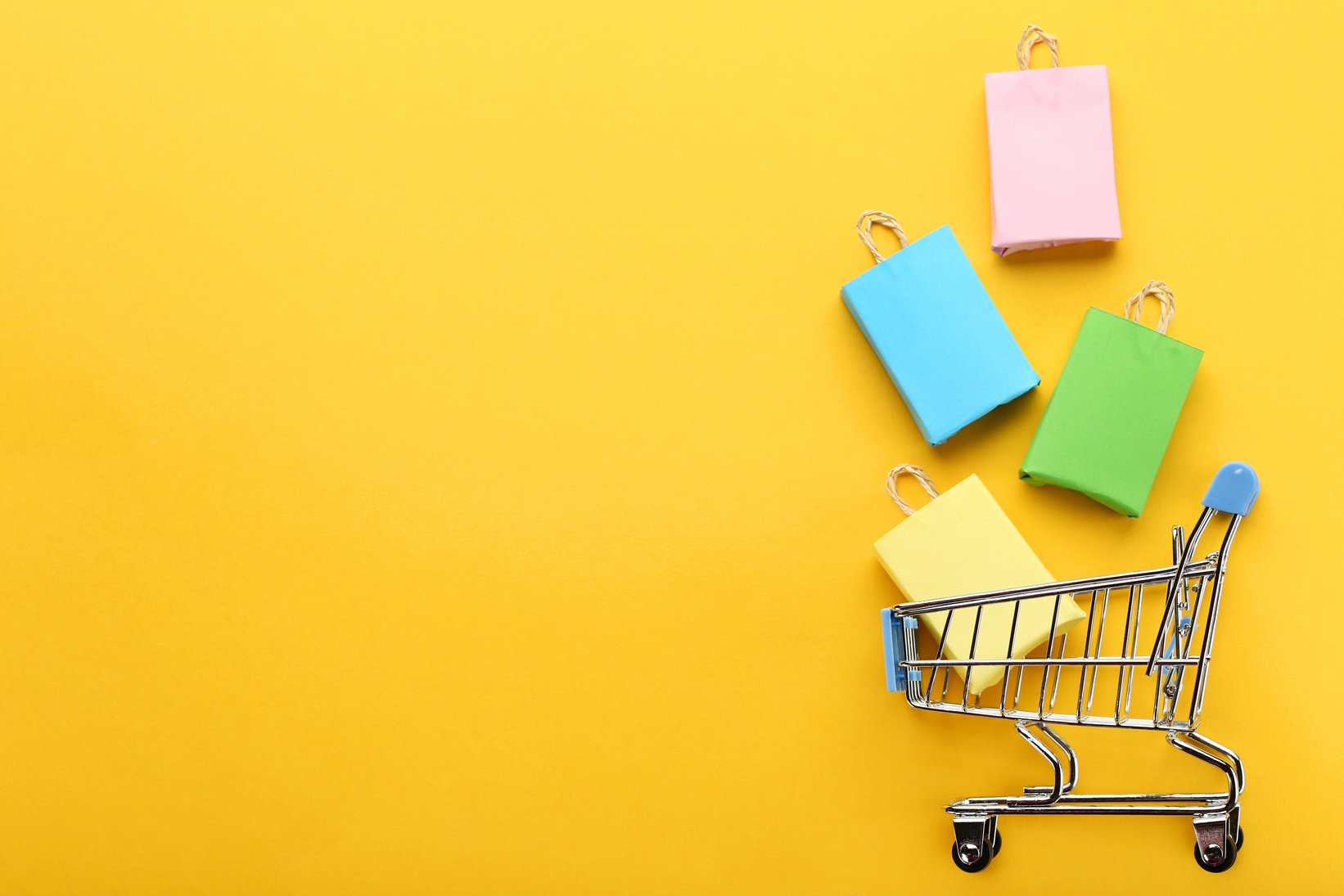 Small paper shopping bags with shopping cart on yellow background